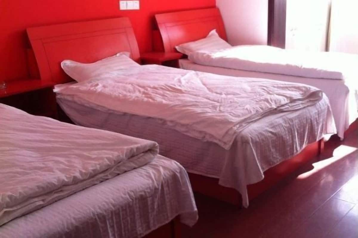 A hotel room with two beds, red headboards, and a window providing natural light.