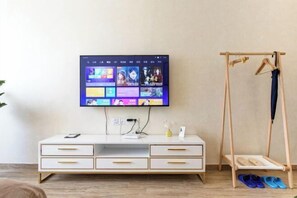 A modern living room with a flat-screen TV mounted on the wall, a white console table with drawers, and a wooden shoe rack with shoes. - suyu hotel (Taiyuan)