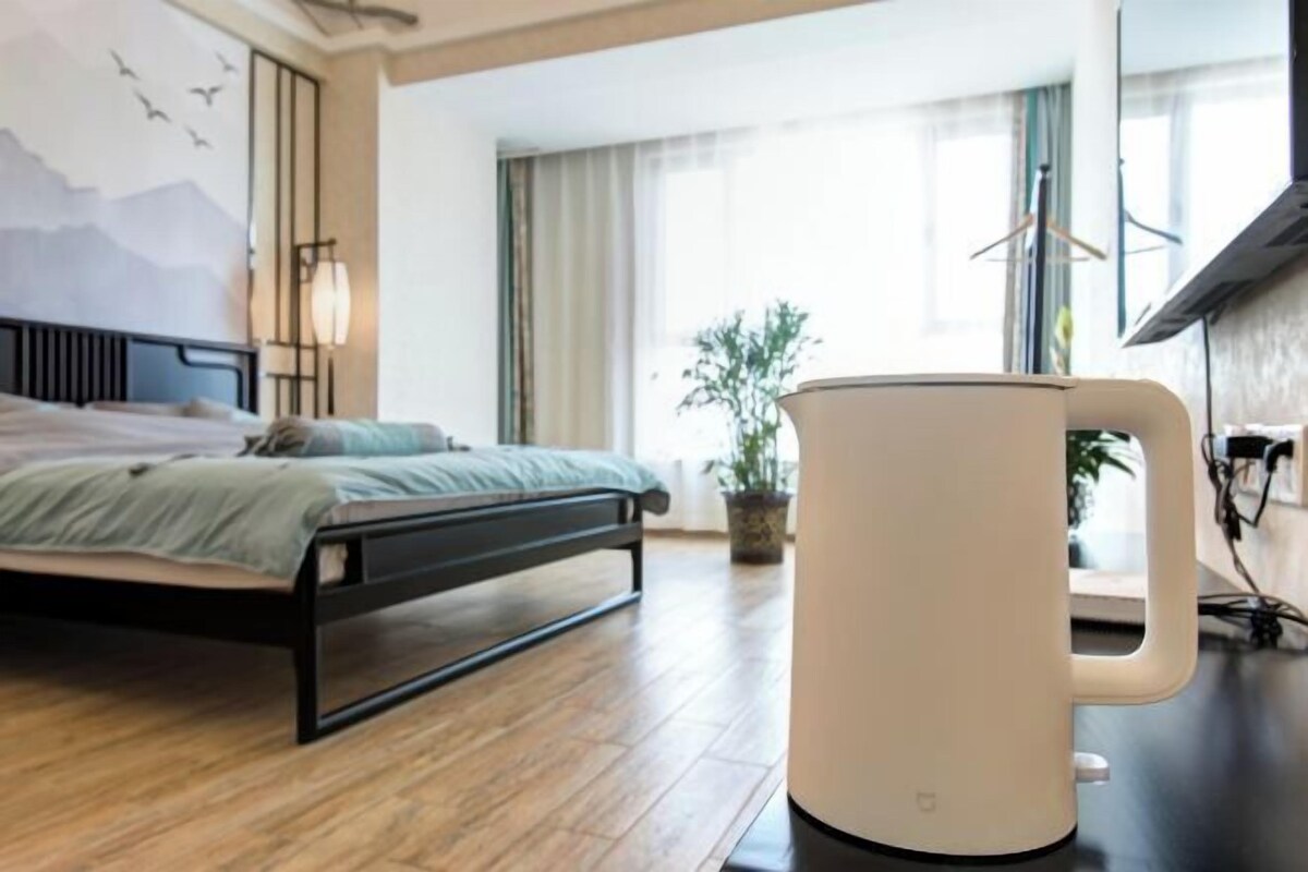 A hotel room with a bed, a large window, a potted plant, and a white coffee maker.