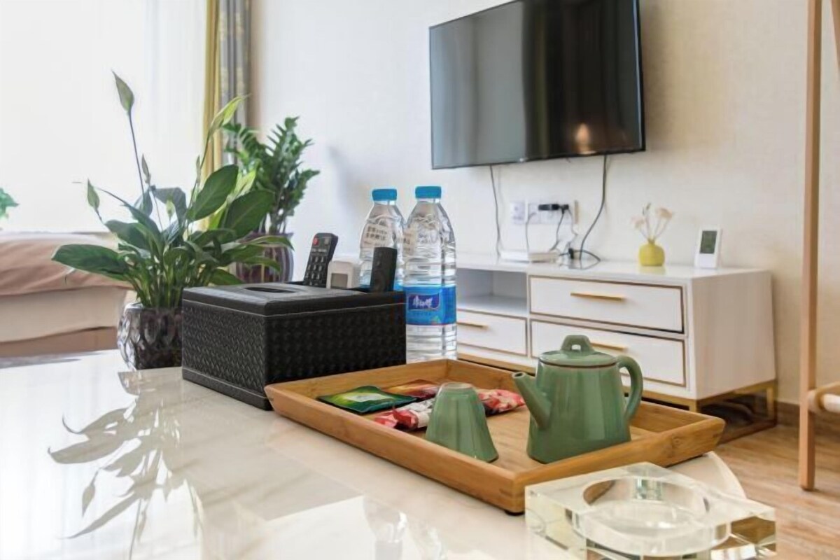 A modern living room with a flat-screen TV, a white dresser, a coffee table with a tray of snacks, a green teapot, and a water bottle.