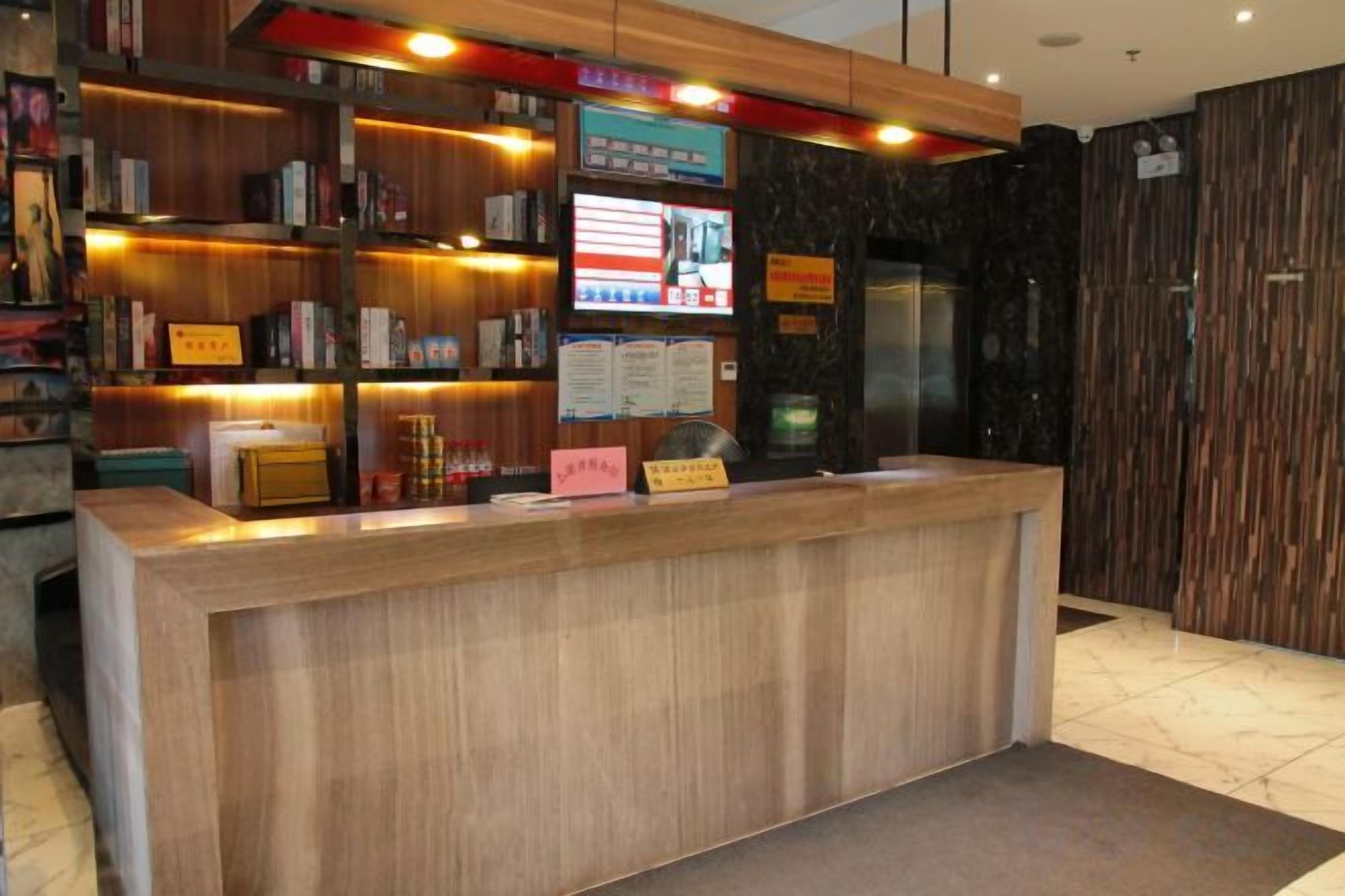 A reception desk with a wooden finish, a digital screen, and a menu board.
