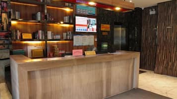 A reception desk with a wooden finish, a digital screen, and a menu board.