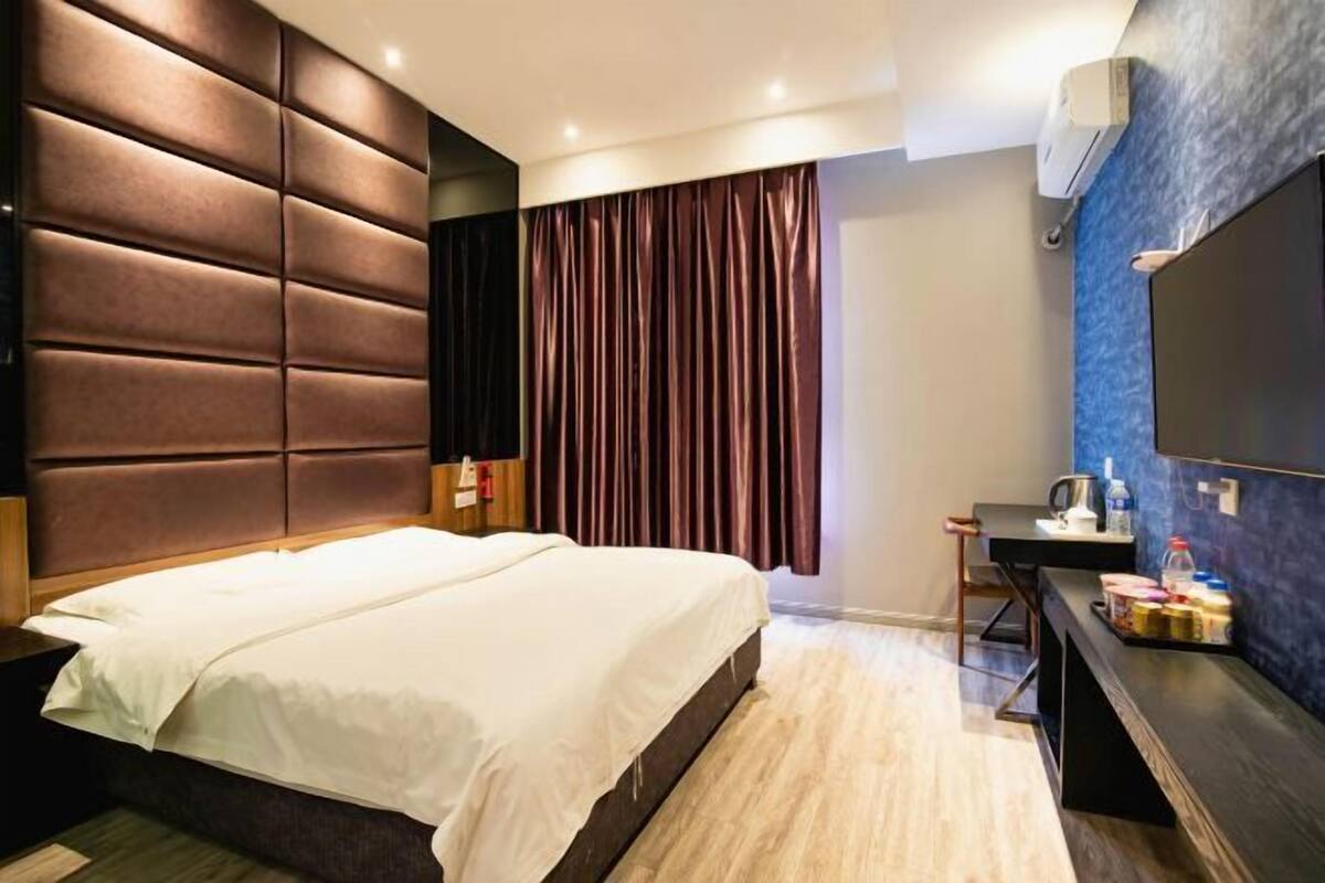 A modern hotel room with a large bed, a flat-screen TV, a desk with a chair, and a window with curtains.