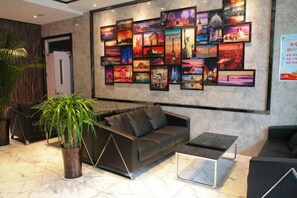 A modern lobby with a black leather sofa, a coffee table, and a large wall of framed pictures. - Gujia Hotel (Xinxiang)