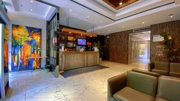 A hotel lobby with a reception desk, seating area, and a large abstract painting.