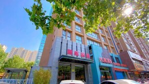 A multi-story building with a prominent entrance, a parking area in front, and adjacent commercial establishments. - Gujia Hotel (Xinxiang)