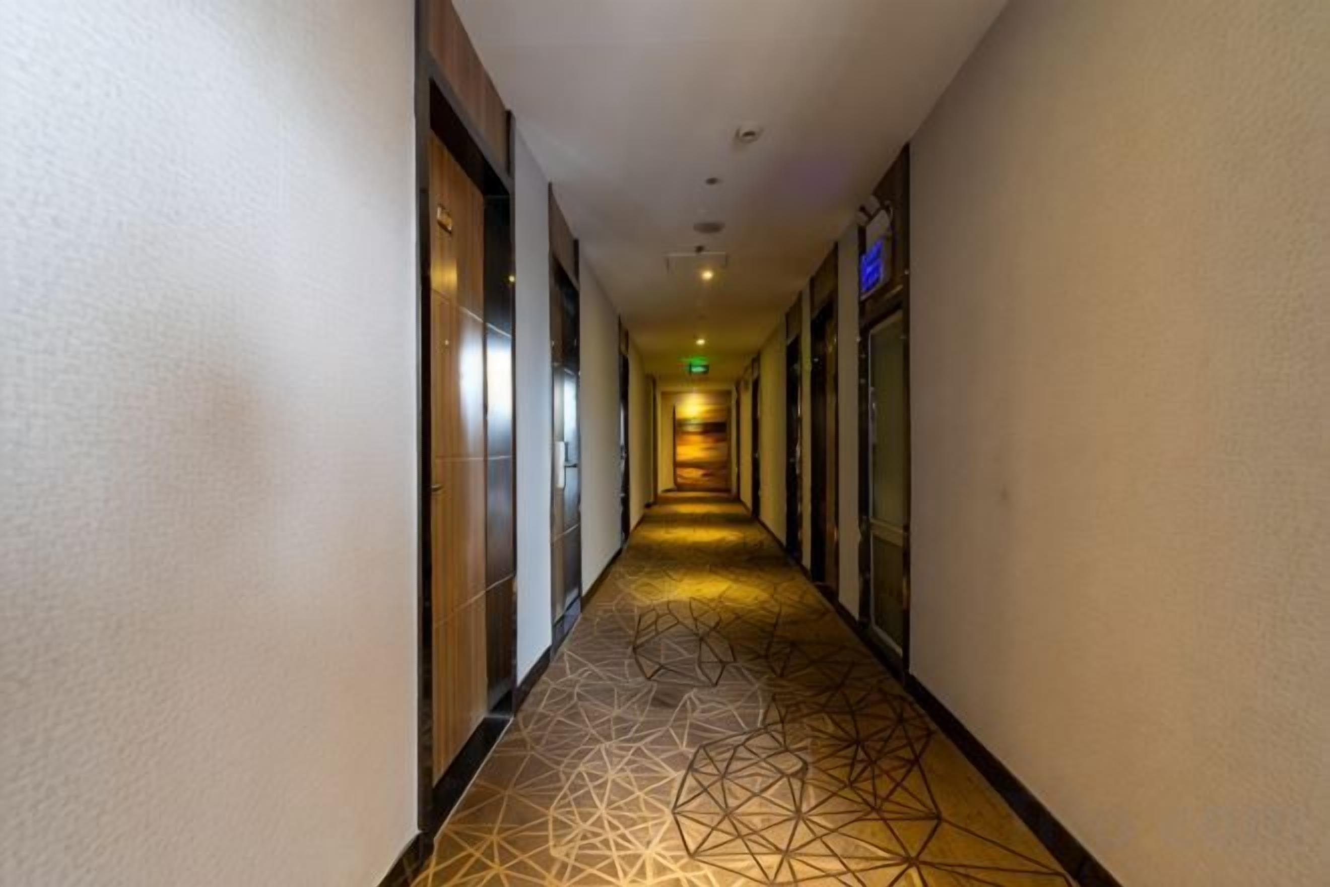 A hotel corridor with doors on both sides, a patterned floor, and a ceiling with recessed lighting.