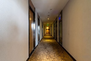 Pasillo de hotel con puertas a ambos lados, suelo estampado e iluminación empotrada en el techo.