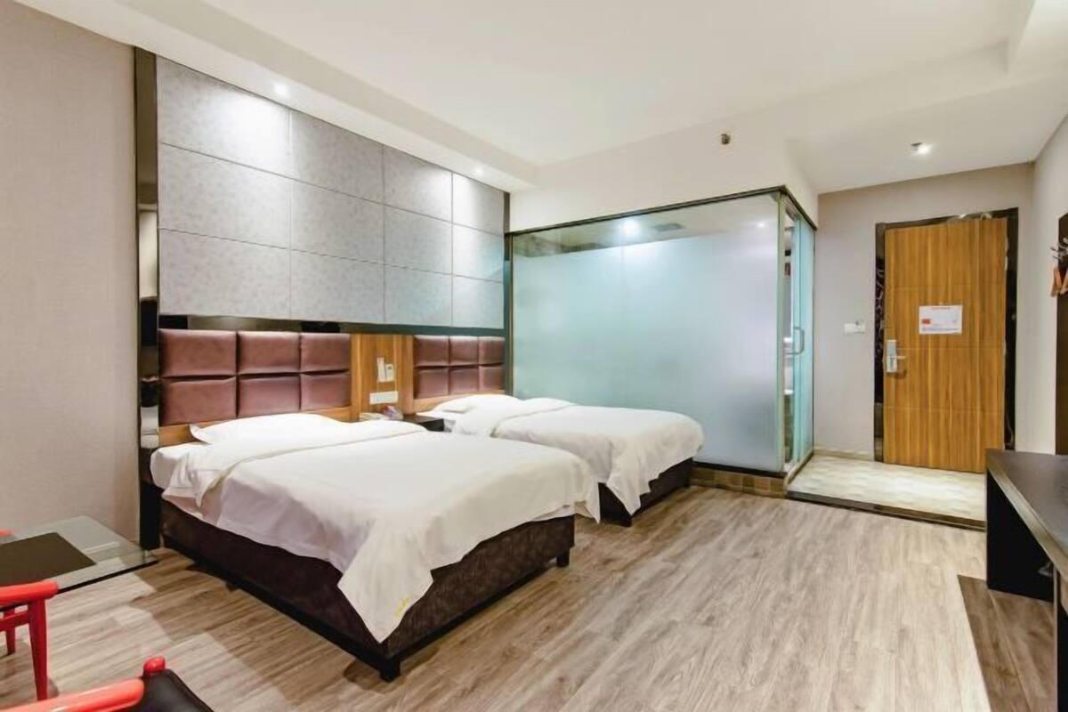A hotel room with a large bed, a glass shower enclosure, and a wooden door.