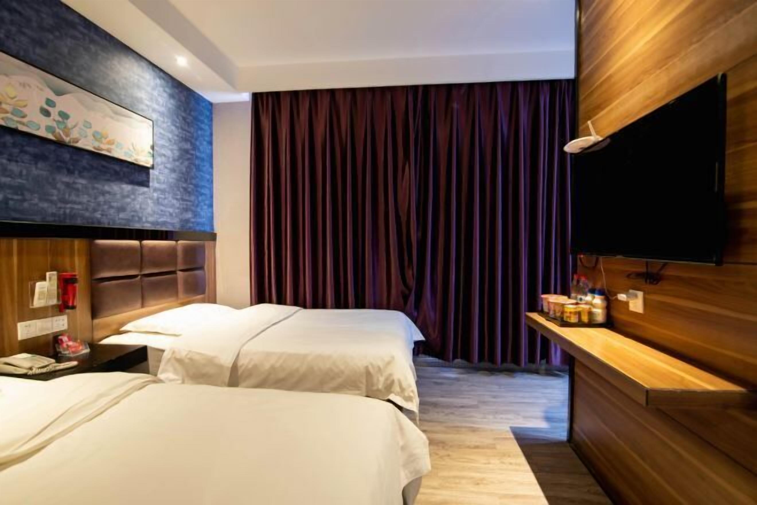 Ett hotellrum med två sängar, en sänggavel i trä, en platt-TV, ett skrivbord i trä och ett stort fönster med gardiner.