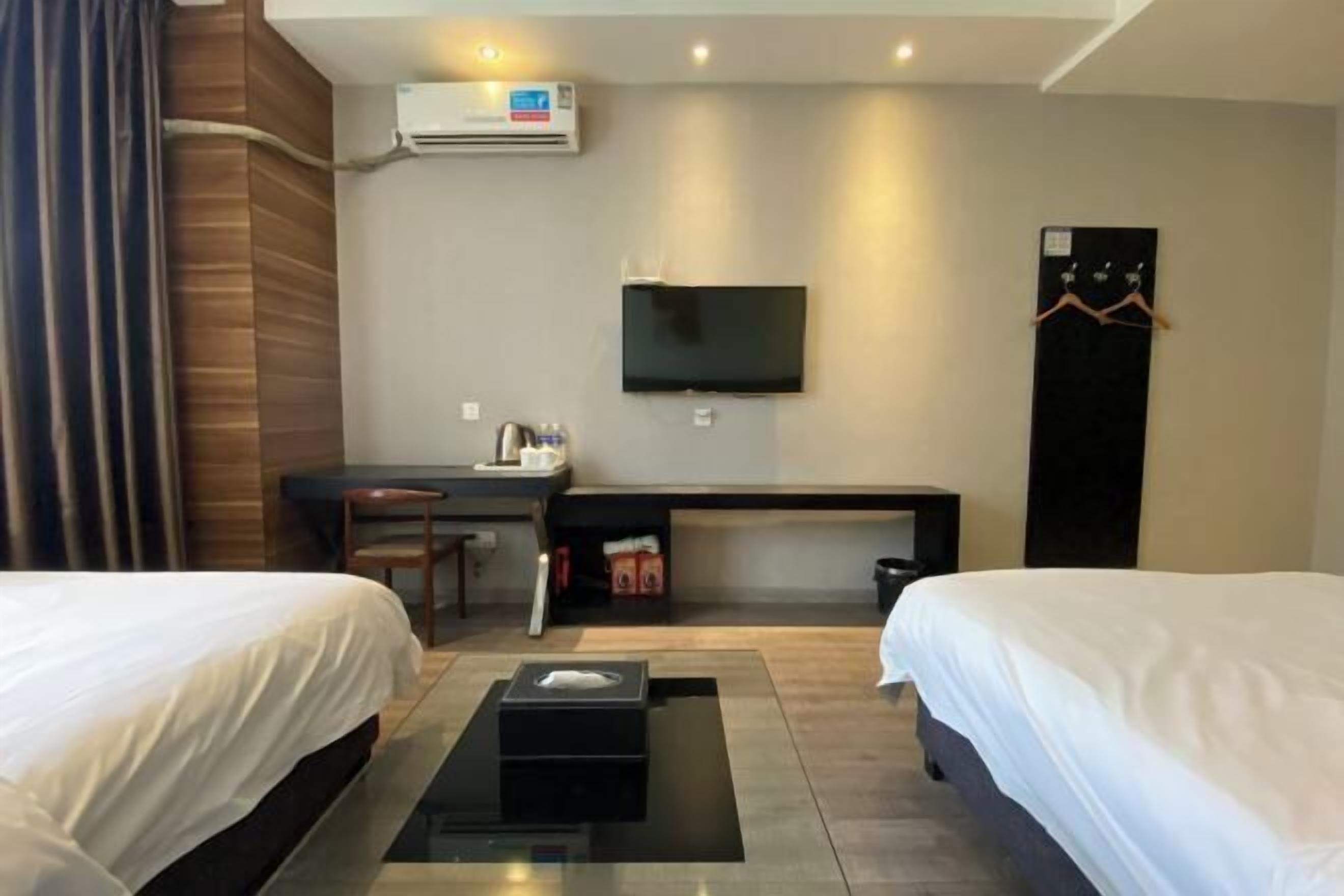 Quarto de hotel com duas camas, uma escrivaninha, uma televisão e um guarda-roupa.