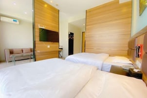 Habitación de hotel con dos camas, un sofá y un cabecero de madera.