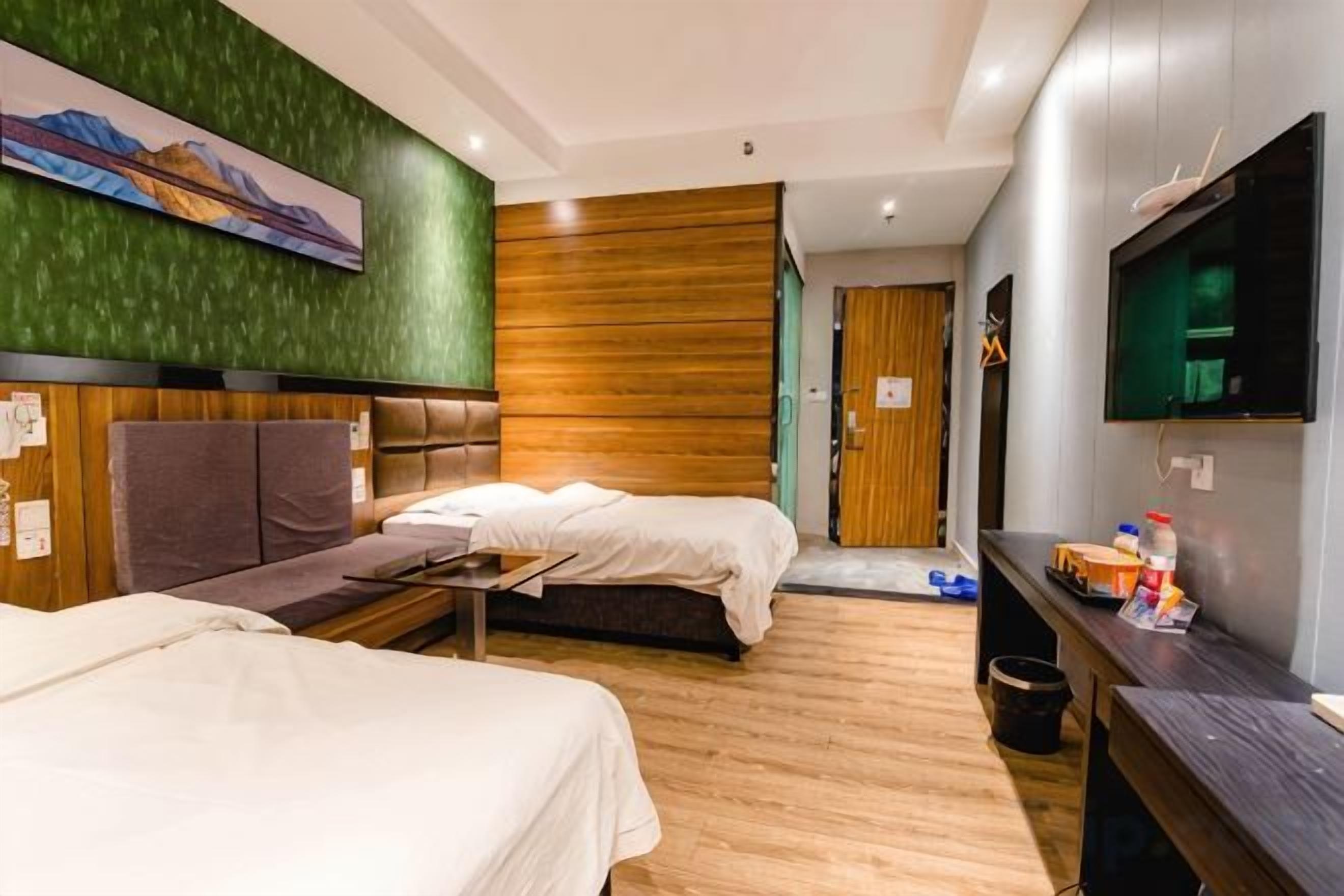 A hotel room with two beds, a sofa, a television, and a wooden wall.