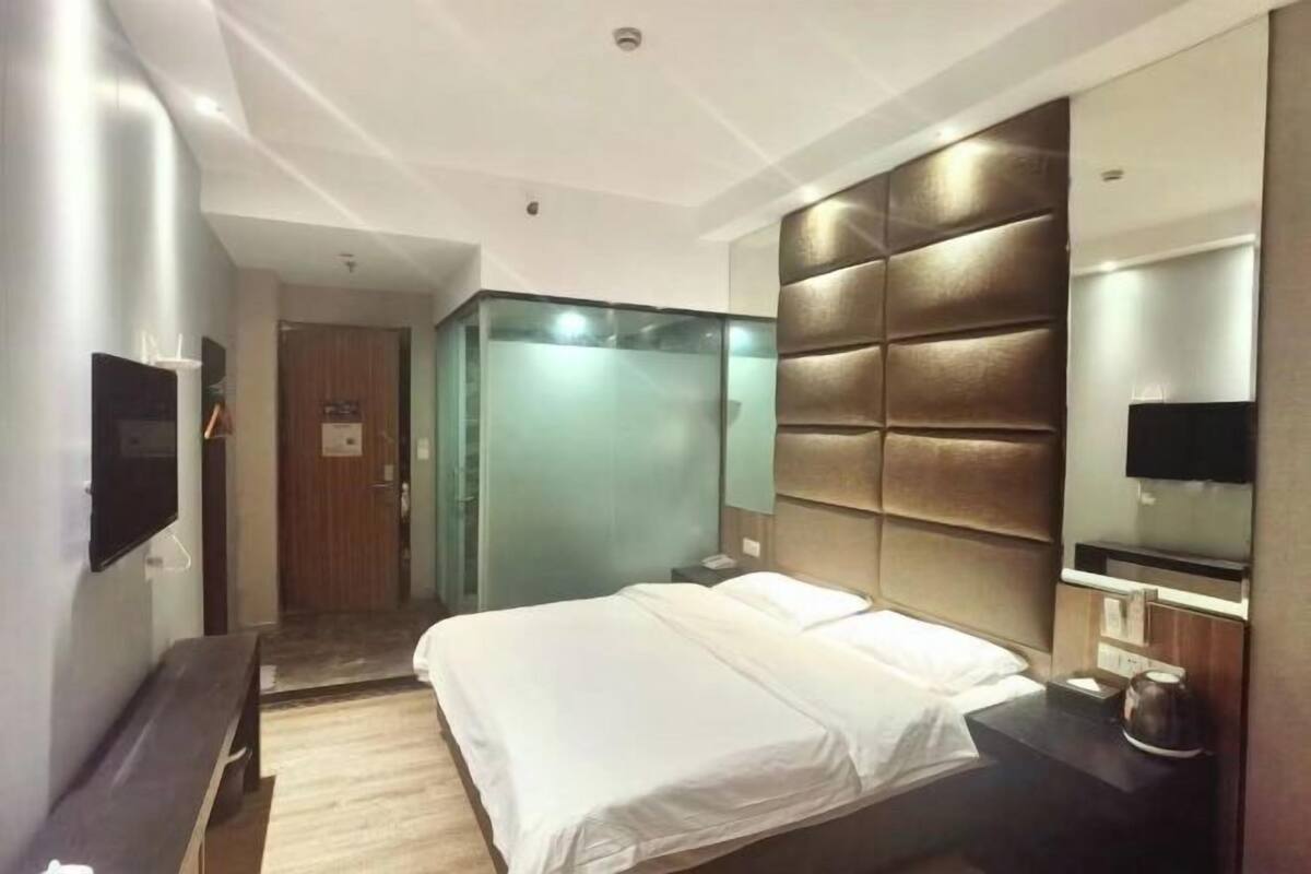 A modern hotel room with a large bed, a flat-screen TV, a bedside table, and a mirror.