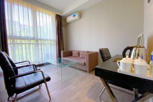 A modern living room with a glass coffee table, a sofa, a black leather chair, and a dining table with white cups and a kettle. - Gujia Hotel (Xinxiang)