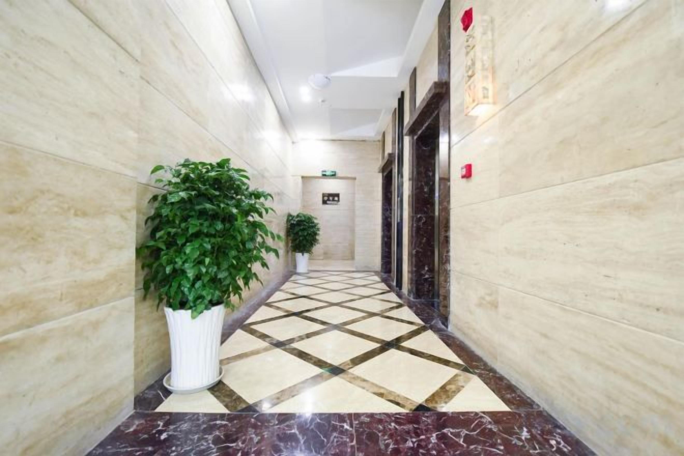 A corridor with marble flooring, potted plants, and a door with a sign.