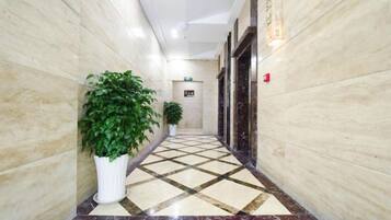 A corridor with marble flooring, potted plants, and a door with a sign.