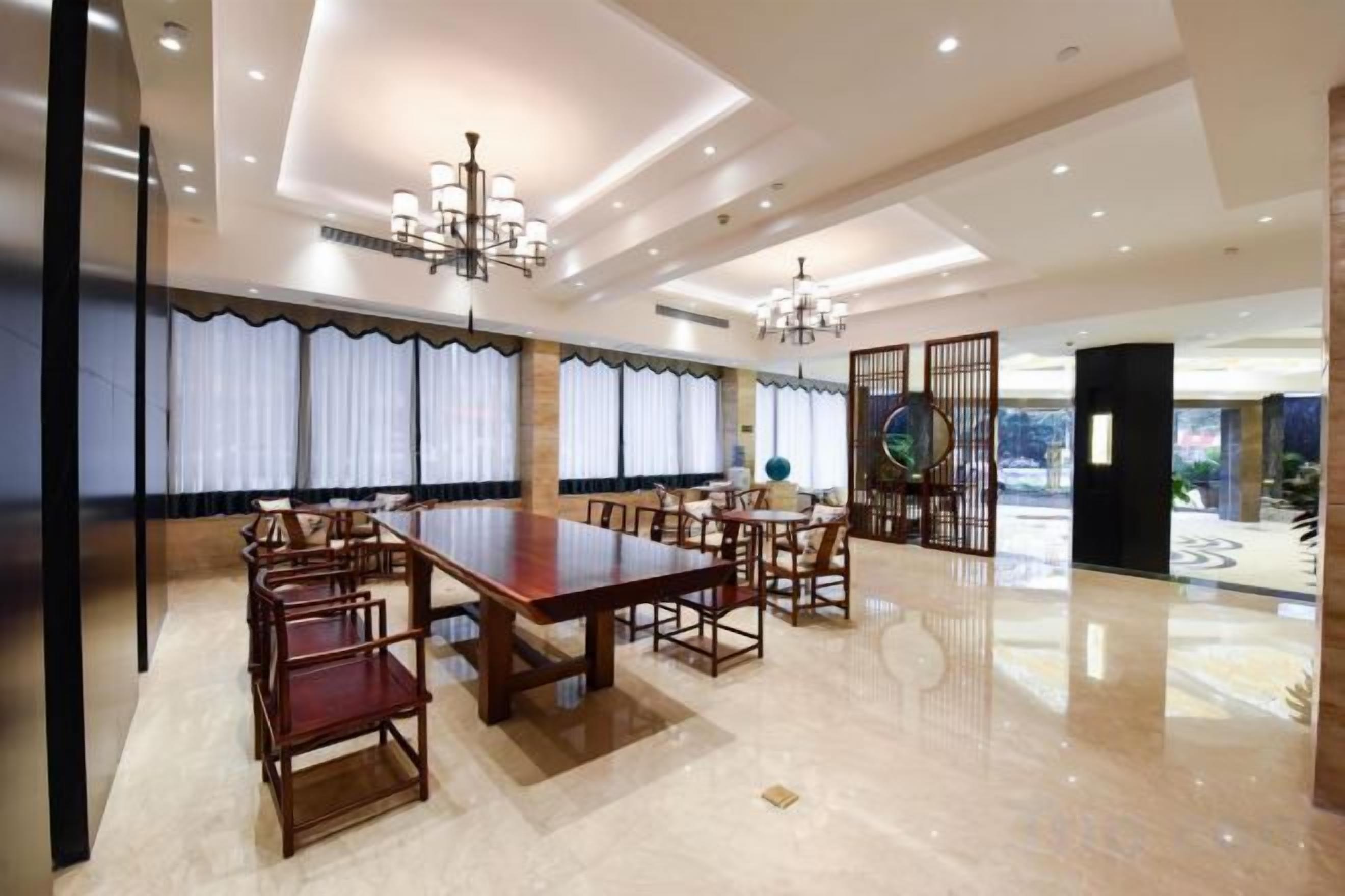 A spacious dining area with a long table and chairs, a chandelier, and a view through a large window with curtains.