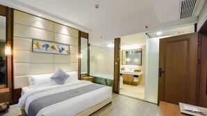 A modern hotel room with a large bed, a bedside table, a desk, a mirror, and a bathroom visible through a glass door. - Chongqing Jinchuan Hotel (Chongqing)