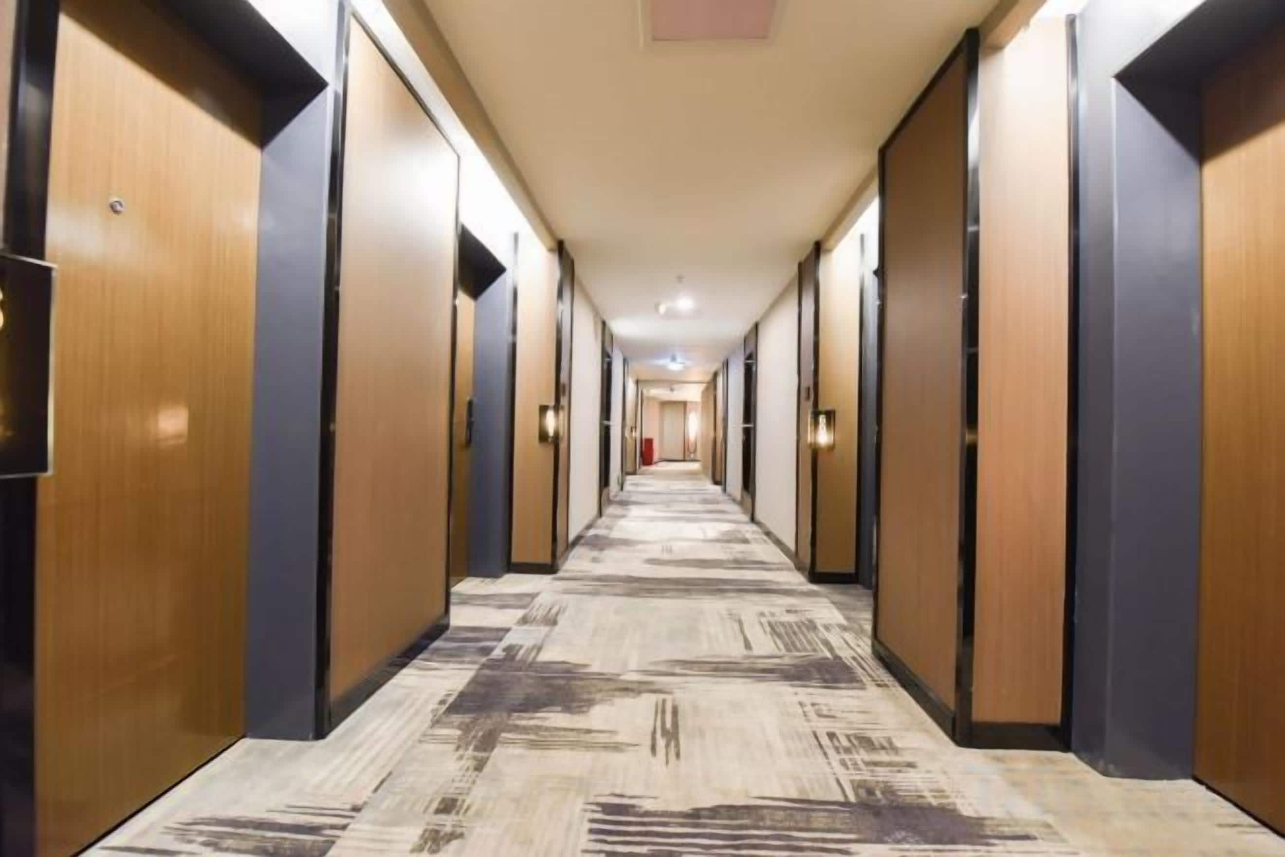Ein Hotelgang mit Holztüren, Teppichboden und Deckenbeleuchtung.