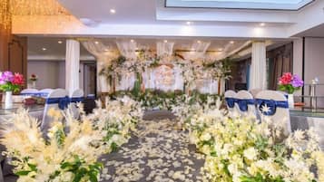 An indoor venue with a floral aisle, seating, and a stage with a backdrop.