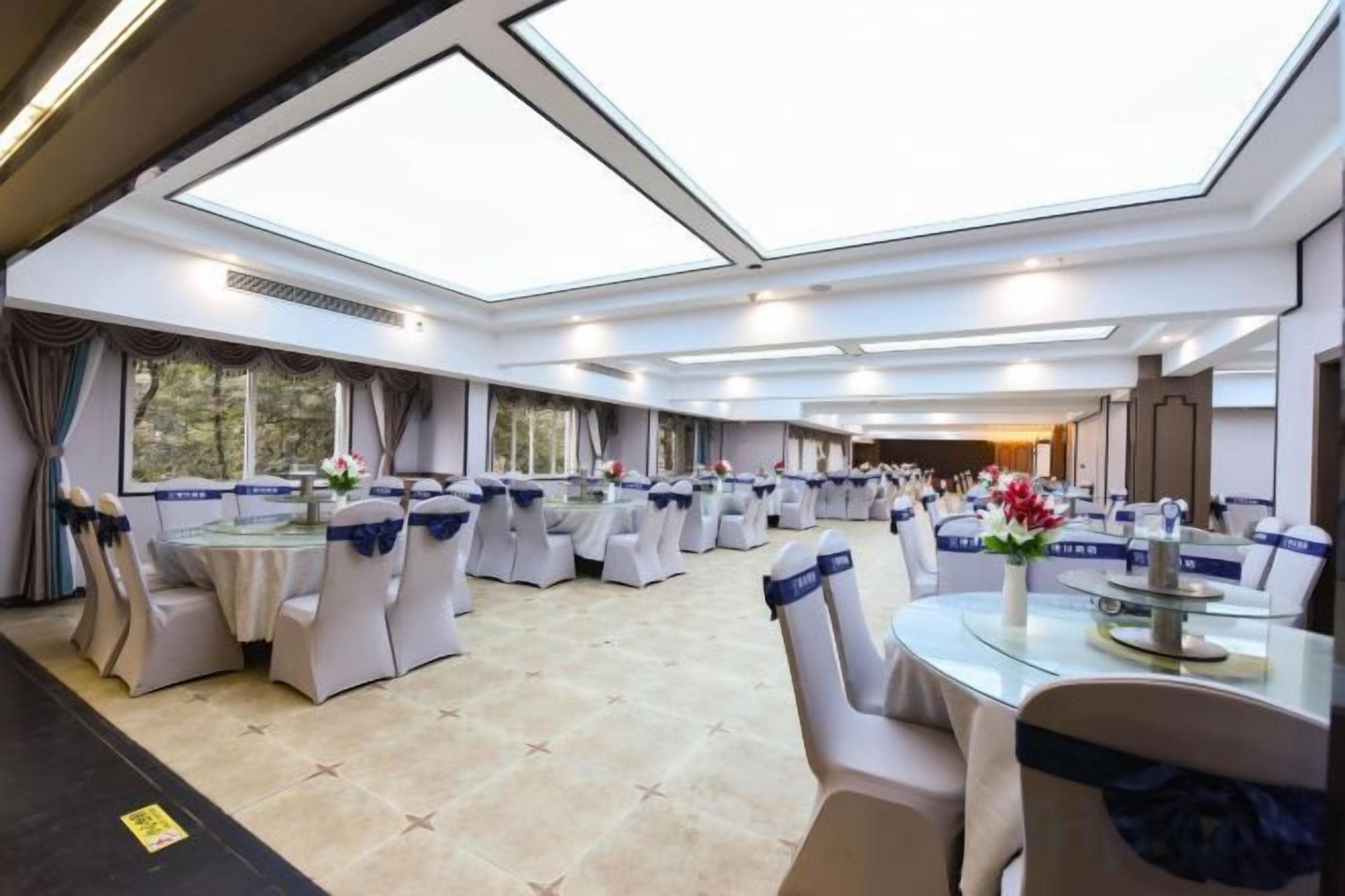 Une salle de banquet avec des tables rondes et des chaises, de grandes fenêtres et un plafond haut.