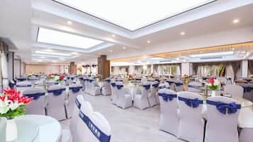 Una vasta sala da banchetti con tavoli rotondi e sedie, soffitti alti e lucernari.