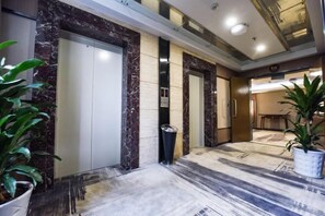 Un vestíbulo de hotel con piso de mármol, dos ascensores y plantas en macetas.