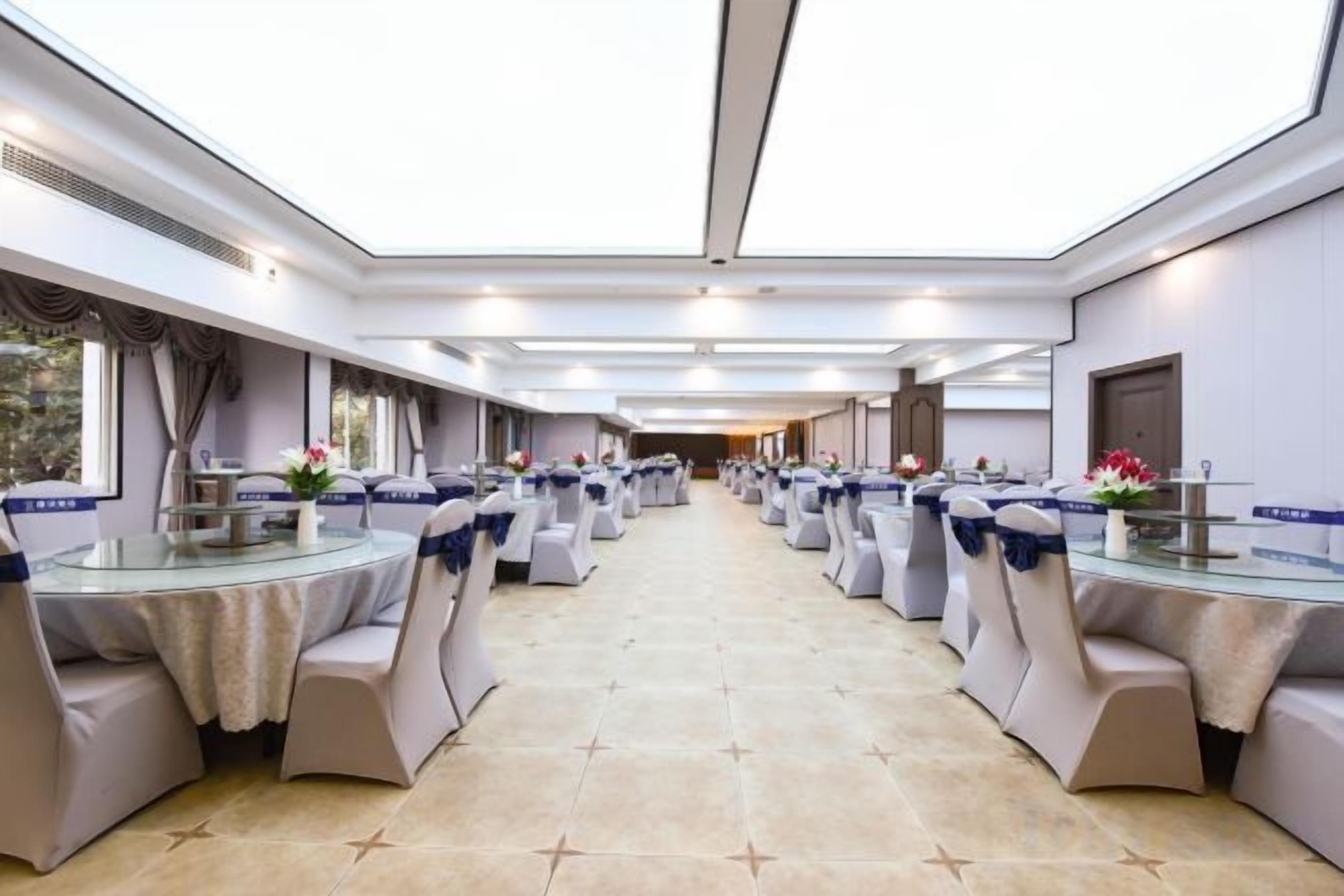 A banquet hall with round tables and chairs, a long table with a buffet, and a view through the ceiling.