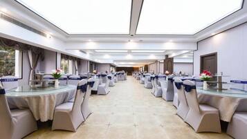 A banquet hall with round tables and chairs, a long table with a buffet, and a view through the ceiling.