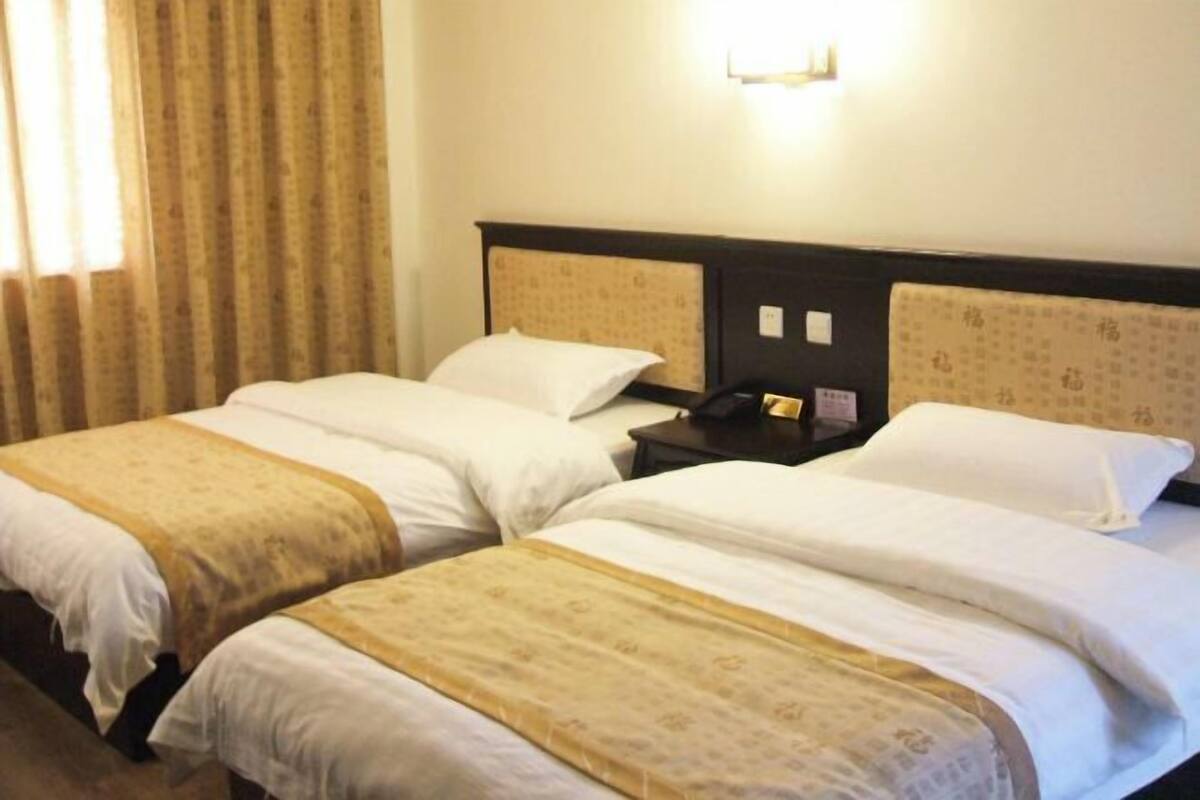 Une chambre d’hôtel avec deux lits, une table de chevet et un luminaire fixé au mur.