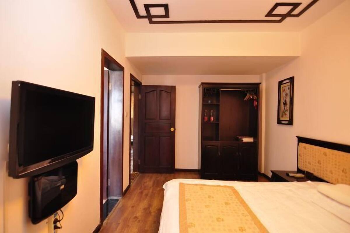 Une chambre d’hôtel avec un lit, un téléviseur fixé au mur, une porte en bois et une petite table avec une lampe.