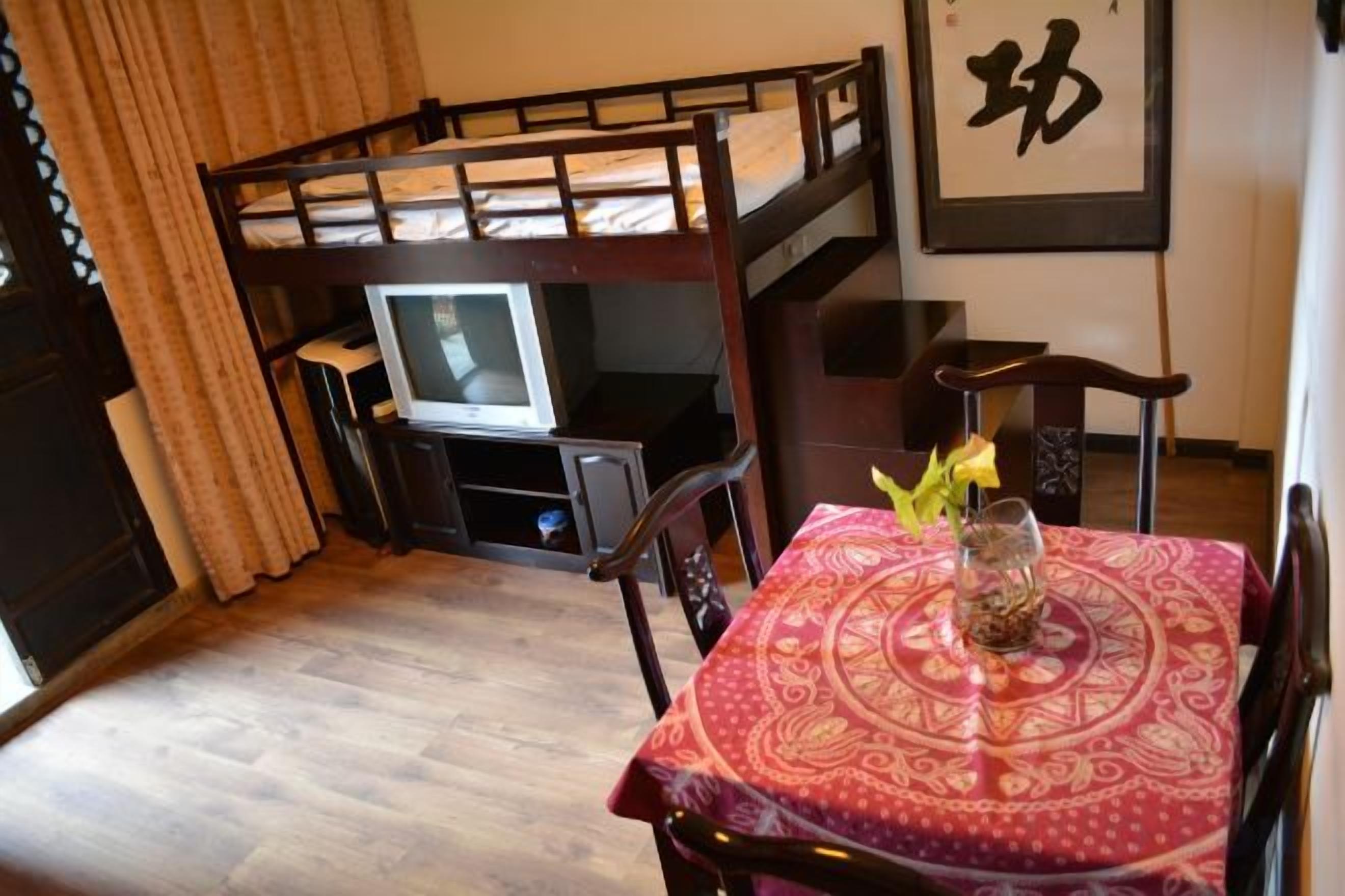 Una stanza con un letto a castello, una televisione, un tavolo da pranzo con una tovaglia fantasia e un vaso decorativo.