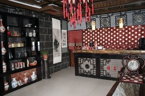 A traditional interior with a black shelving unit displaying pottery, a red and white patterned counter, and a hanging red lantern.