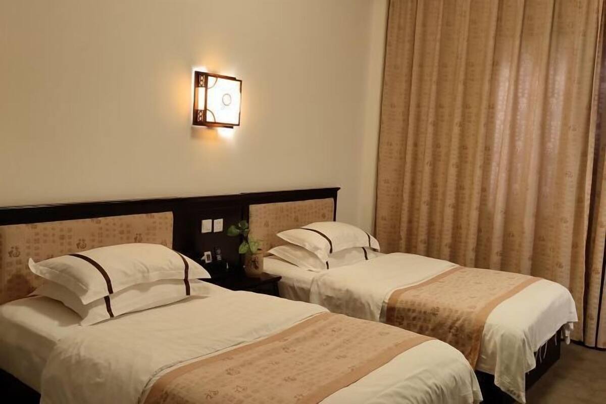Une chambre d’hôtel avec deux lits, une table de chevet, une lampe fixée au mur et un rideau.