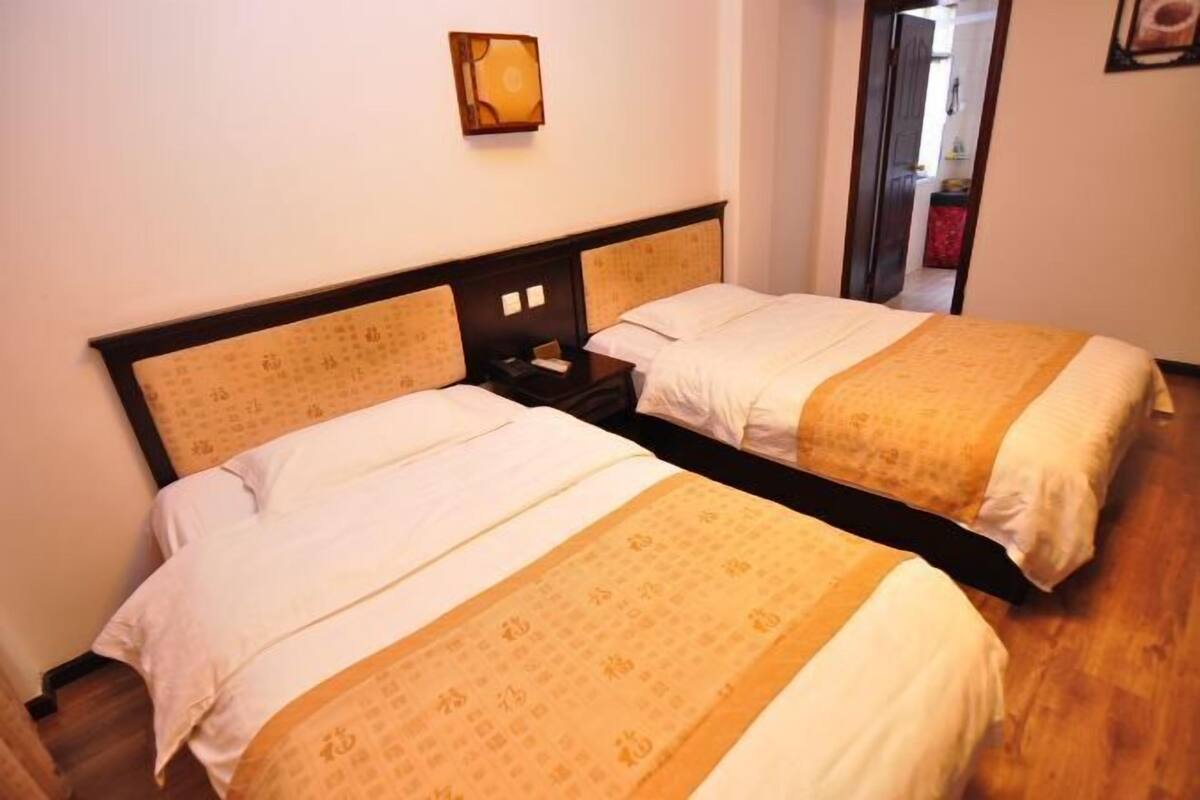 Deux lits simples avec des têtes de lit, une table de chevet et un luminaire fixé au mur.
