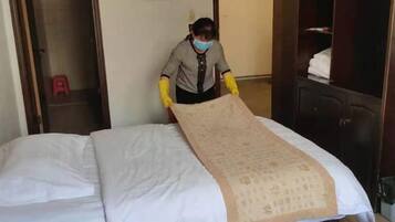 Eine Person legt eine Tagesdecke auf ein Bett in einem Hotelzimmer.
