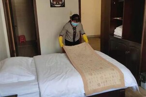 Uma pessoa colocando um cobre-leito sobre uma cama em quarto de hotel.