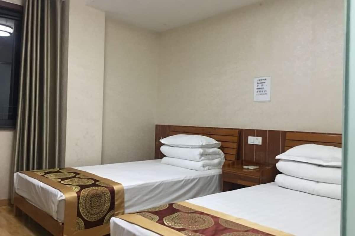 A hotel room with two single beds, a wooden headboard, a nightstand, and a window with curtains.
