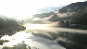 Un lago sereno con montañas al fondo y niebla elevándose desde el agua.