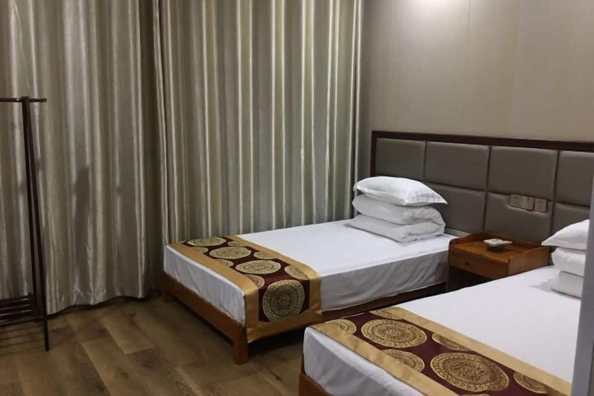 A hotel room with two beds, a wooden floor, a headboard, and a curtain.