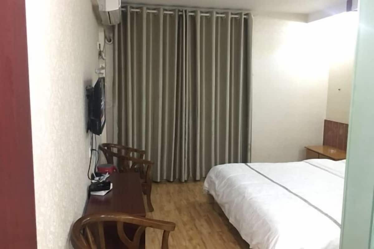 A hotel room with a bed, a desk with chairs, a television, and curtains.