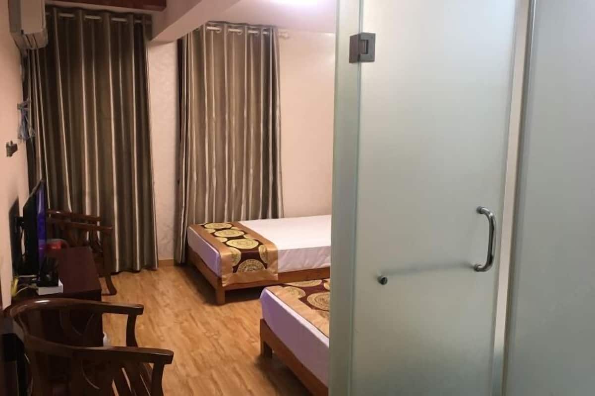 A hotel room with two beds, a desk, a chair, and a door.
