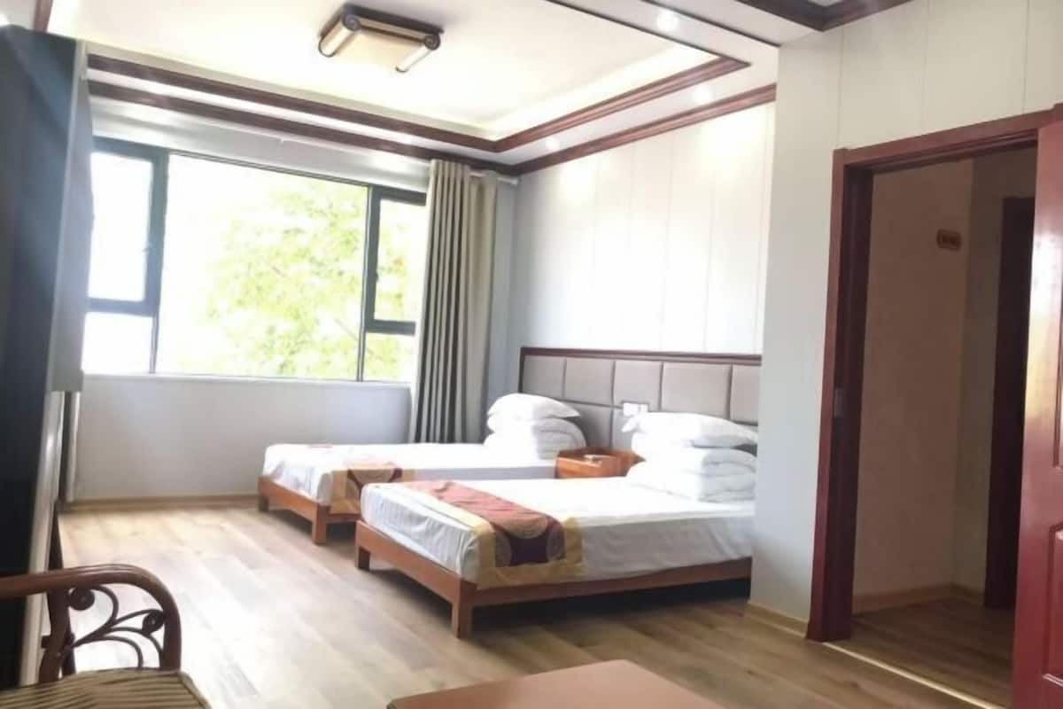 A hotel room with two beds, a wooden floor, a window with curtains, and a door.