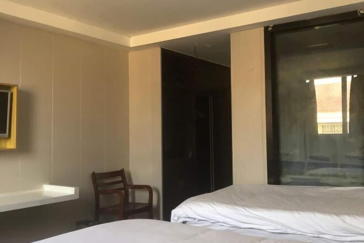 A hotel room with a bed, a chair, a TV mounted on the wall, and a large window.