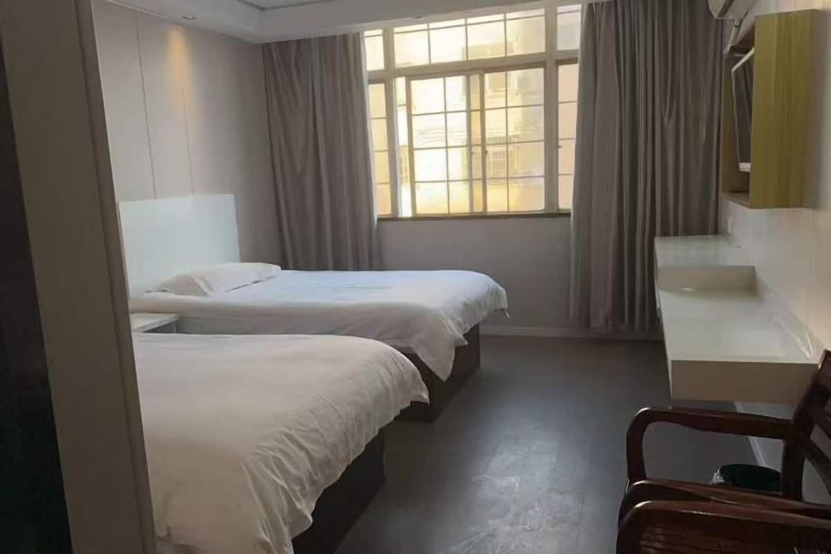 A hotel room with two beds, a desk, and a window with curtains.