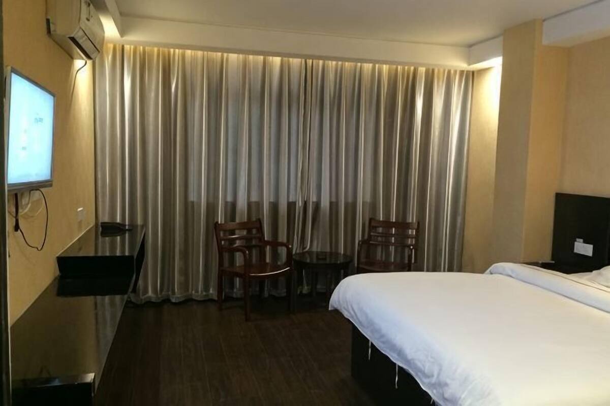 A hotel room with a bed, a desk, a chair, a small table, and a TV.