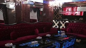 Ein Zimmer mit einem rot gepolsterten Sofa, einem Glastisch mit blauen Mustern und einer Chandelüster.