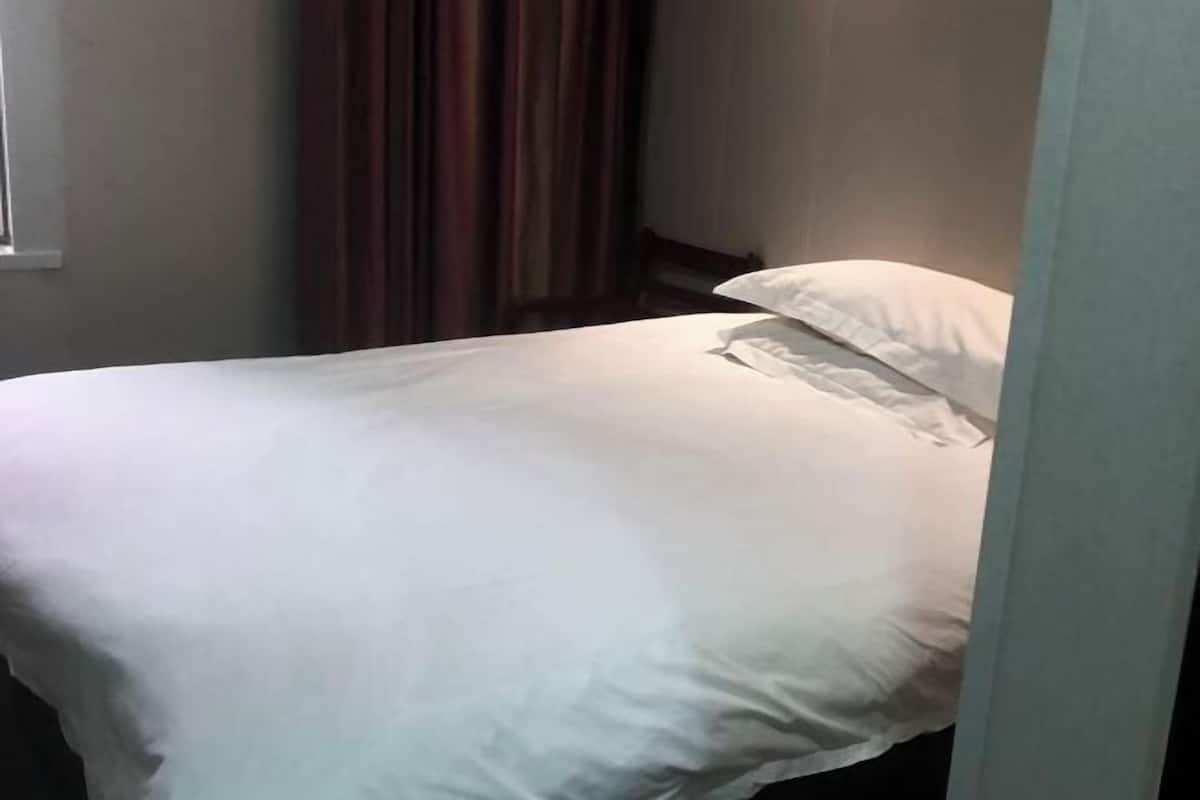 A bed with white bedding in a room with a window and curtains.