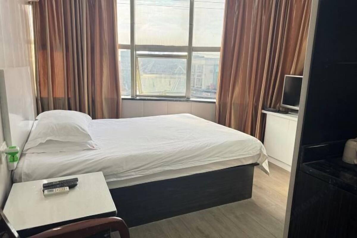 A hotel room with a bed, a bedside table with a remote control, a TV, and a window with curtains.